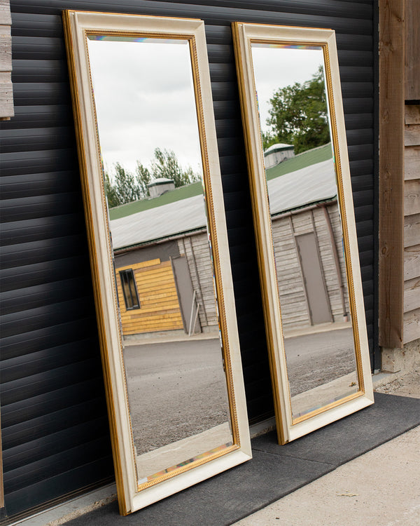 Two tall mirrors lean against a garage door. The mirror glass is bevelled and framed using an aged cracked gesso finish with antique gold detailing. 