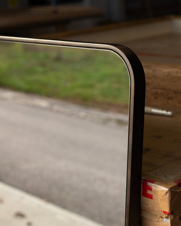 A close up photo of the thin bronze frame and radial corner of this bespoke Nutbourne Mirror. 