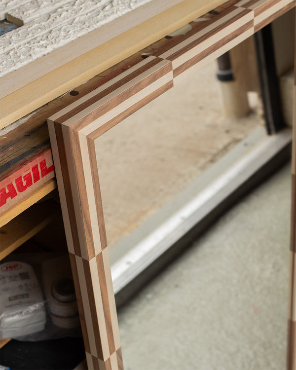The corner of a mirror, framed using a two-colour veneer Chequered design in light grey sycamore and walnut. 