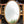 An oval mirror leaning against a work bench in a workshop. The frame is finished in an imitation brass and a bobbin detail runs along the inside of the frame. The mirror glass is lightly antiqued with heavier antiquing along the edges. The mirror is reflecting a grey sky and part of a tree. 
