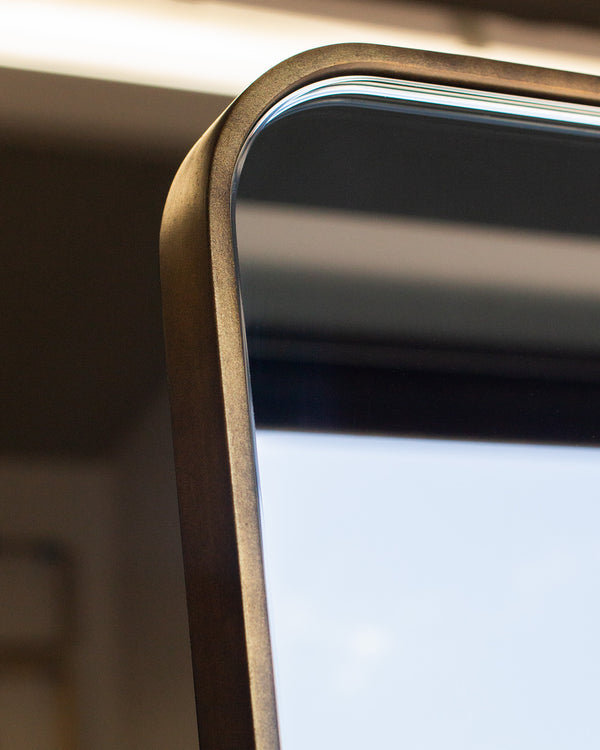 The rounded corner of a mirror. The frame is an imitation antique brass colour, and the thin frame measures 6mm wide. 